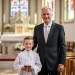 Dědeček a vnuk v kostele při první svaté přijetí, stojí spolu, drží modlitební knihu.