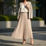 Žena ve městě v béžské plisované sukni a bílé košili, jednoduchý outfit s lodičkami a minimalistickými doplňky